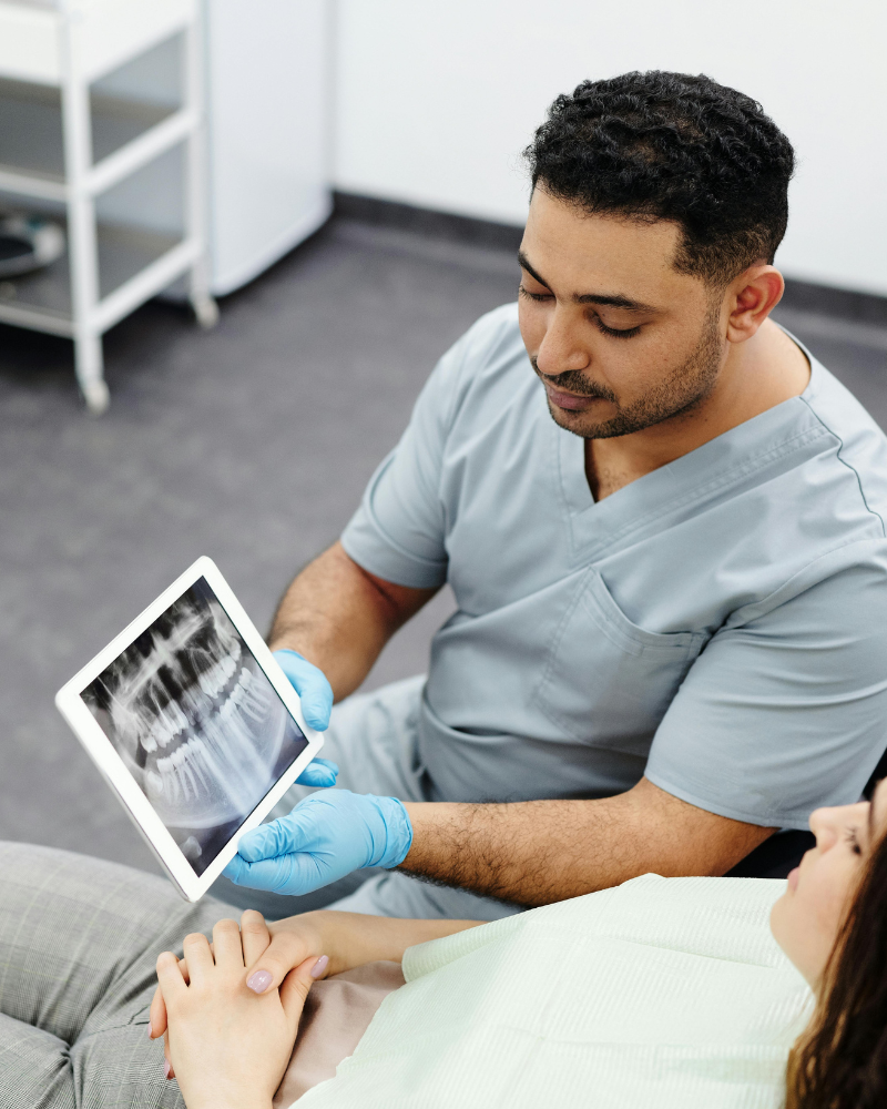 Dentalmediziner bespricht Röntgenbild auf Tablet mit Patientin
