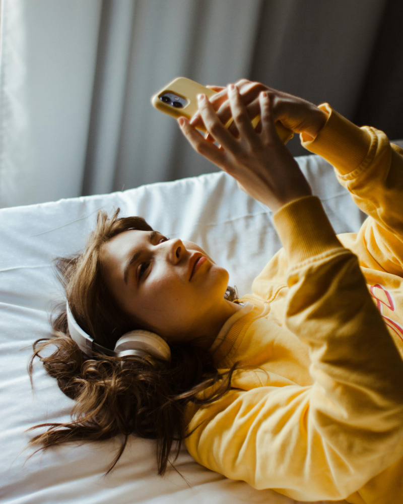 Person liegt mit Kopfhörern im Bett und tippt auf ihr Smartphone