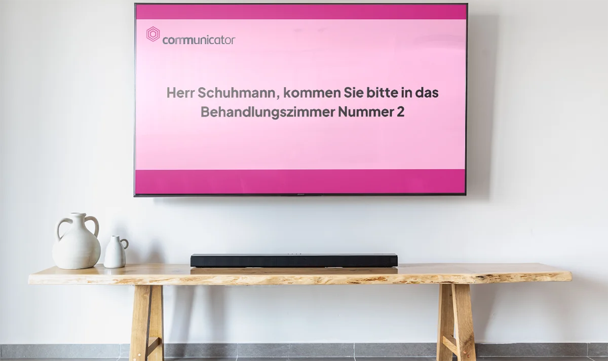 Ein TV hängt an einer Praxiswand mit einem Patientenaufruf in Textform
